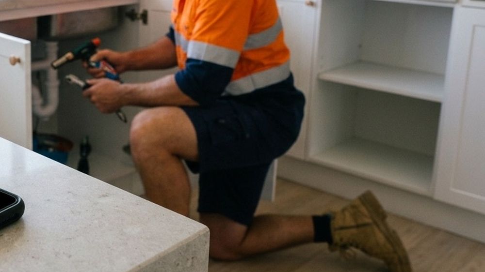 A plumber's hands working on pipes under a sink